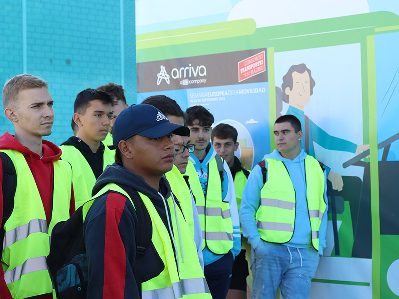 Un grupo de jóvenes con chalecos reflectantes, junto a un cartel con un dibujo que representa un autobús con el logo de Arriva