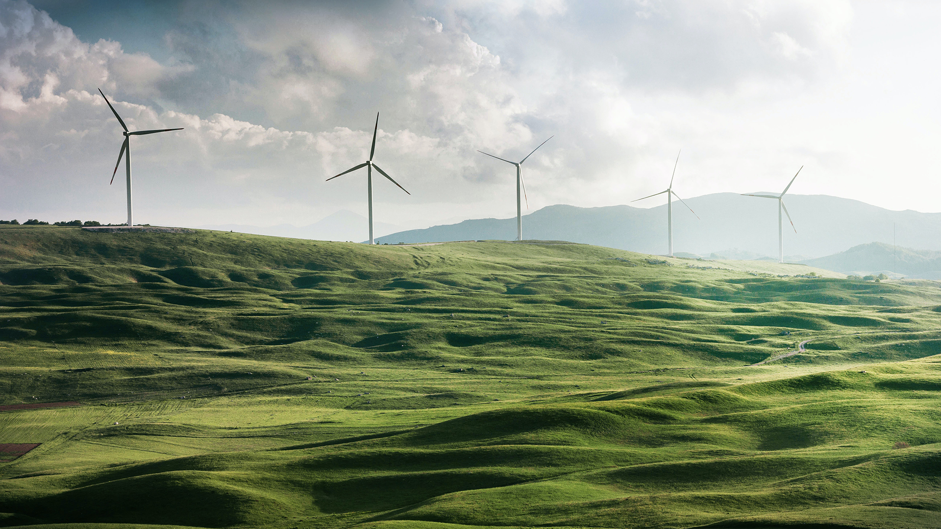 Molinos de energía eólica en un prado verde con montañas al fondo.