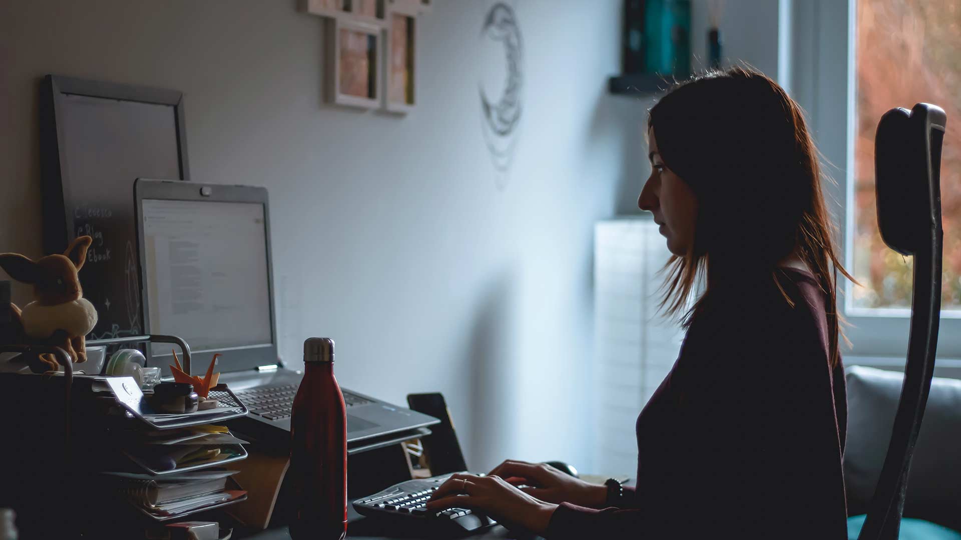 Una mujer trabaja en una mesacon un portátil y un teclado externos, en lo que parece ser un salón.