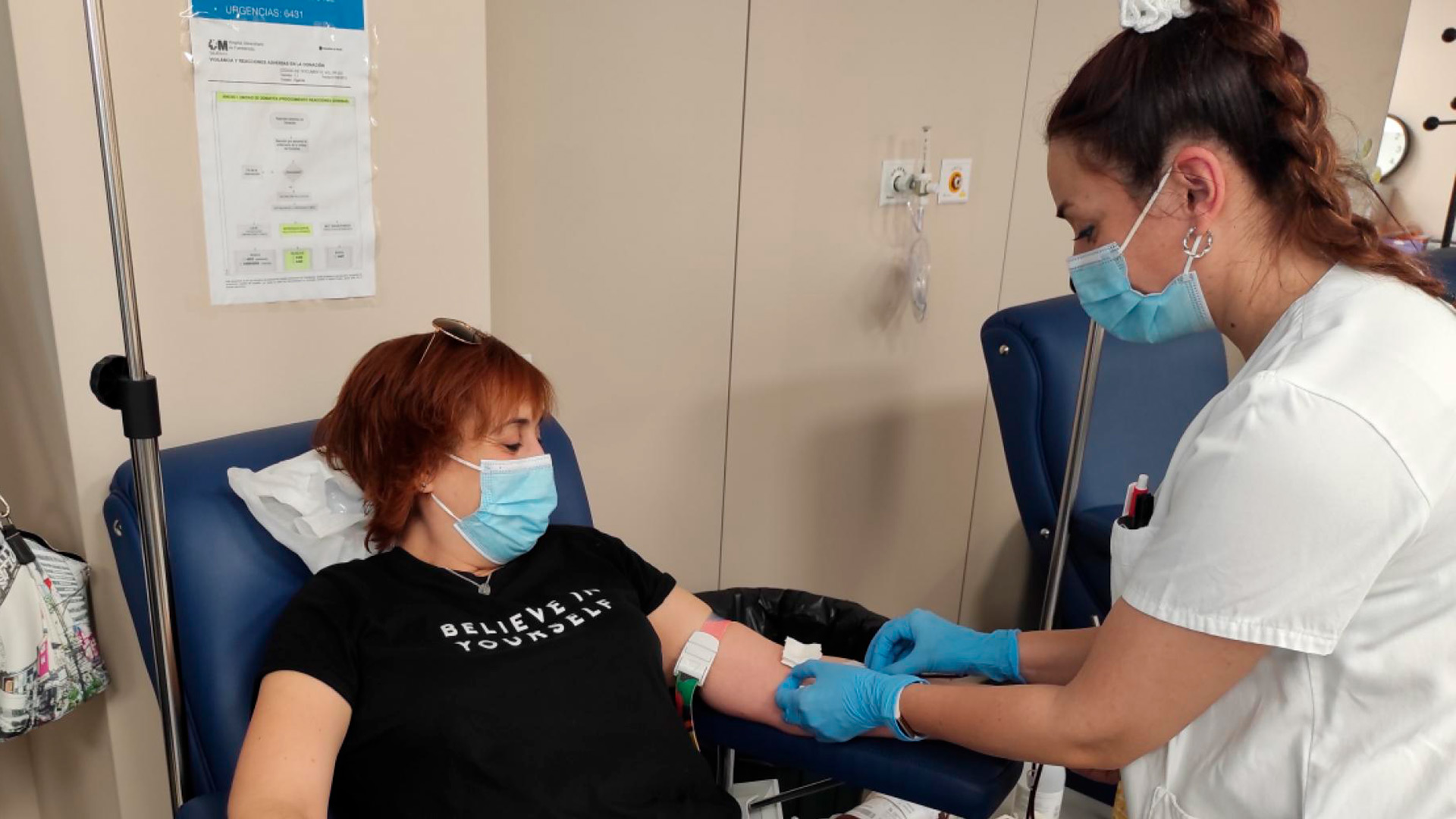 Una mujer sentada en un sillón mira cómo la enfermera le saca sangre para su donación.